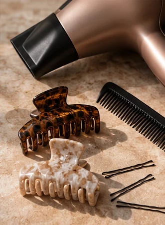 Illustrative hair dryer, hair clips, comb, and hairpins on a stone surface.